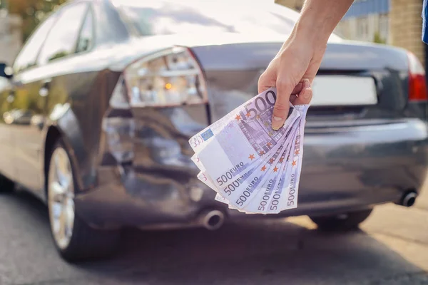 Elinde bozuk bir arabanın arka planında 500 Euro 'luk banknot paketi vardı. Sigorta tazminatı kavramı.