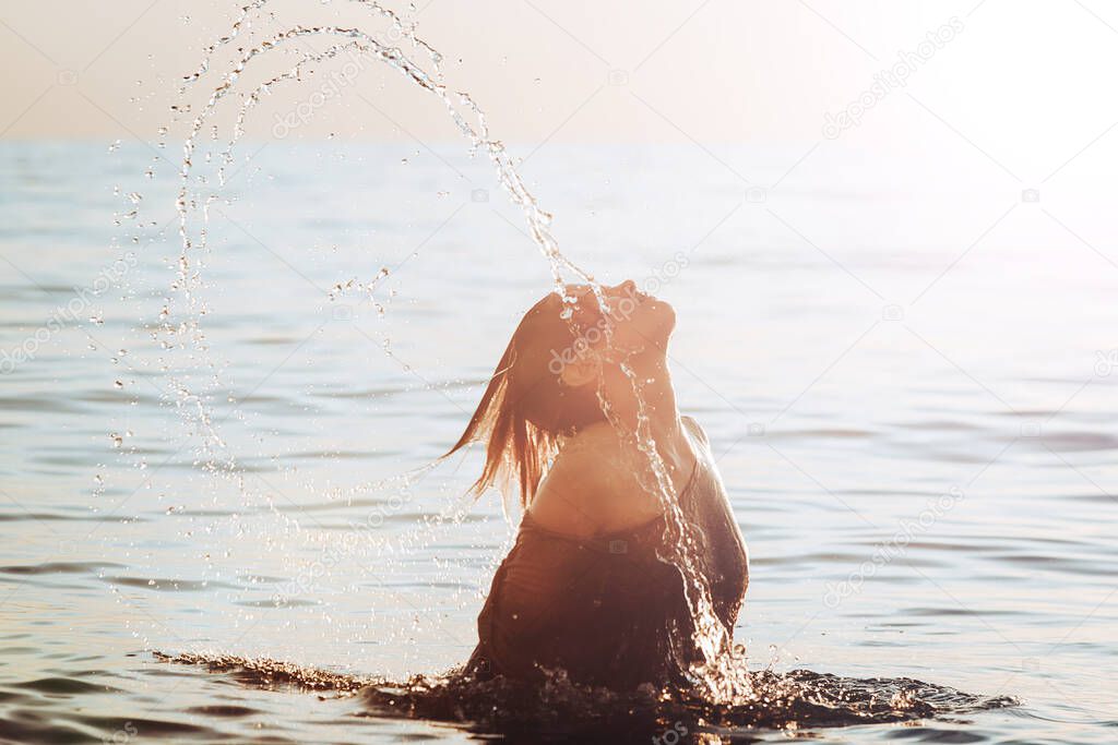 silhouette of a Girl jumping out of the water against the sunrise on the horizon, creating a jet of water hair. The concept of leisure, lifestyle and good mood. 