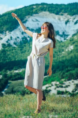 Güneş gözlüklü çekici bir kız dağlık bir bölgede yürüyüş yaparken güneşli ve keyifli bir günün tadını çıkarıyor..