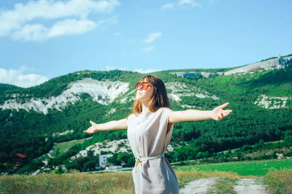 An attractive girl in sunglasses on a walk in a mountainous area enjoys a Sunny day and a good mood.
