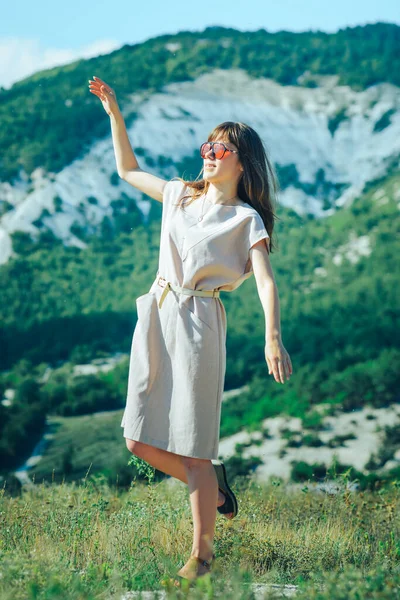 An attractive girl in sunglasses on a walk in a mountainous area enjoys a Sunny day and a good mood.