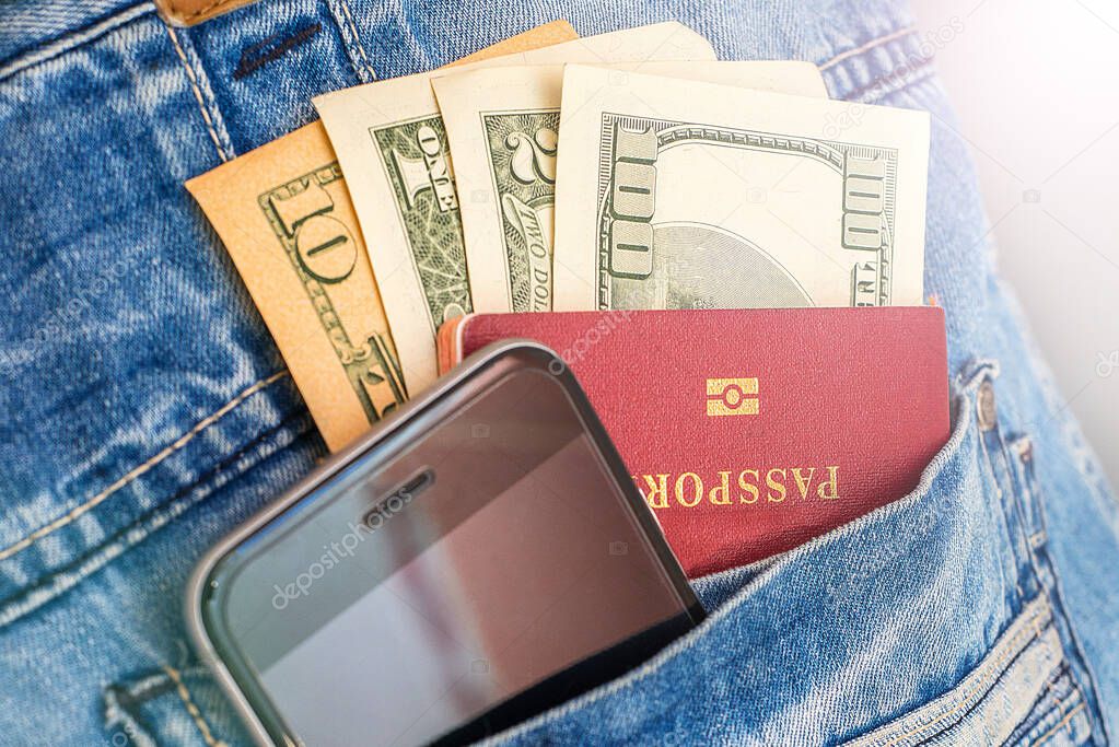 Cash bills stick out of the pocket with a mobile phone and passport. The concept of travel.