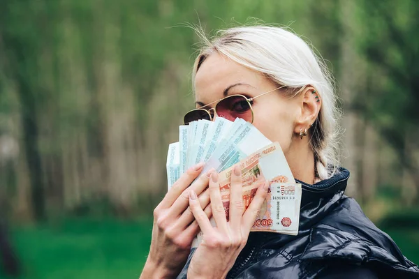 blonde girl made a fan out of a pack of rubles and hid her face bragging about money.