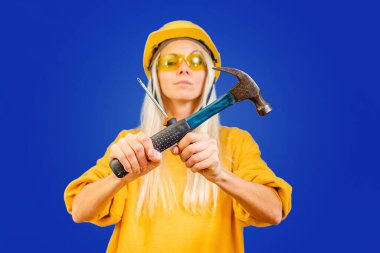 Mavi arka planda kafasında bir kask ve aletle marangoz kız..