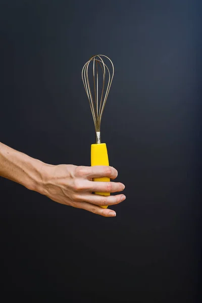 Kitchen accessories. Hand holding beaters for whipping, close - up on black background.