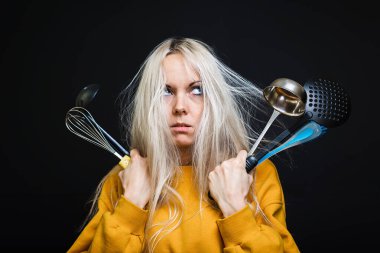 Dağınık saçlı genç bir kız mutfak aletleri tutuyor ve hiçbir şey pişiremeyeceği korkusuyla buraya geliyor. Genç ev hanımı konsepti.