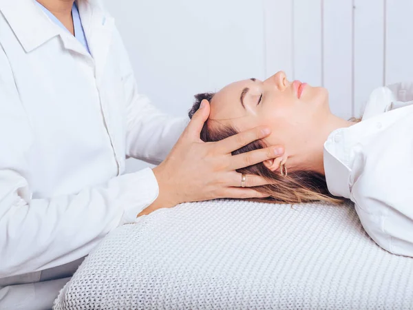 Bir osteopat ile doktor randevusunda olan genç bir kız, boyun bölümlerinin omurgasının eğimini tedavi ediyor..