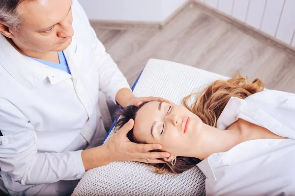 Bir osteopat ile doktor randevusunda olan genç bir kız, boyun bölümlerinin omurgasının eğimini tedavi ediyor..
