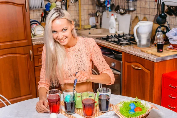 A young attractive girl in the kitchen in the process of coloring Easter eggs, is in a happy mood preparing a surprise for her family.