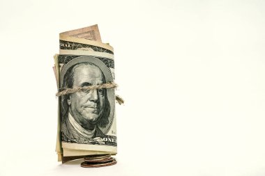 100 dolarlık banknotlar bir boruya sarılır, keten kabloyla bağlanır, küçük bir madeni paranın üzerinde durur, beyaz arka plan..