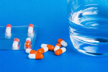 Mavi zemin üzerinde bir bardak su bulunan tıbbi kapsüller. Sağlık kavramı.