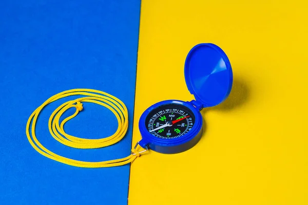 Blue compass with yellow thread lies on yellow-blue the surface.