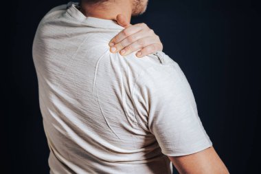 Adam elini omzuna koydu, siyah arka planda duruyordu. Travma, romatizma, akut ağrı kavramı..