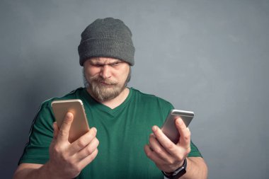 Yünlü şapkalı bir gencin portresi sohbet başlatmak için hangi cep telefonunu seçeceğini seçmeye çalışıyor..