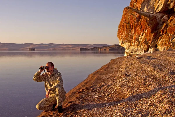 Homem olha através de binóculos na costa do Lago Baikal — Fotografia de Stock