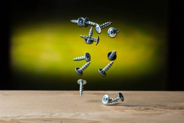 Tahta bir arka planda kontrplak üzerine düşen kendi kendine dokunan vidalar, siyah, krom ve sarı