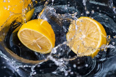 Siyah arka planda damlalar ve su damlaları olan koca bir limonu yarıladılar.