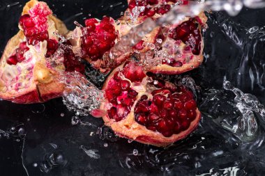 kırmızı nar meyvesi, akıntılı ve siyah arkaplanda biraz su.