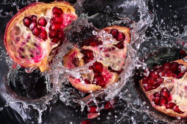 kırmızı nar meyvesi, akıntılı ve siyah arkaplanda biraz su.