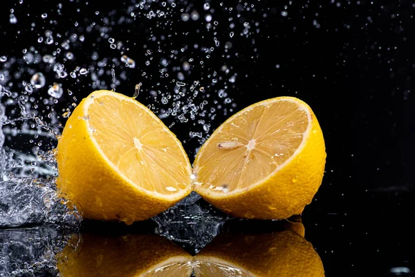 Siyah arka planda damlalar ve su damlaları olan koca bir limonu yarıladılar.