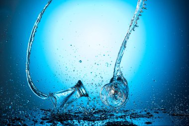 Düşen ve zıplayan kadehler mavi bir arkaplanda bir damla su ya da votka ile