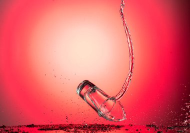 Uçan bir şarap bardağına su veya kırmızı gradyan arka planda votka sıçratır.