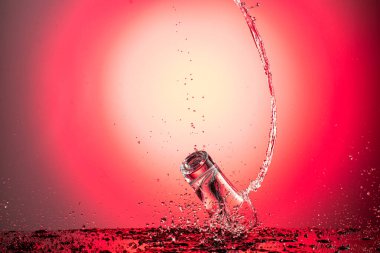 Uçan bir şarap bardağına su veya kırmızı gradyan arka planda votka sıçratır.