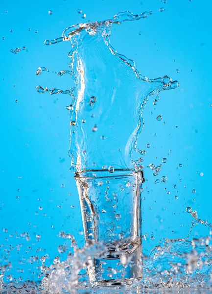 在蓝色底色的玻璃杯中泼洒纯净水 — 图库照片