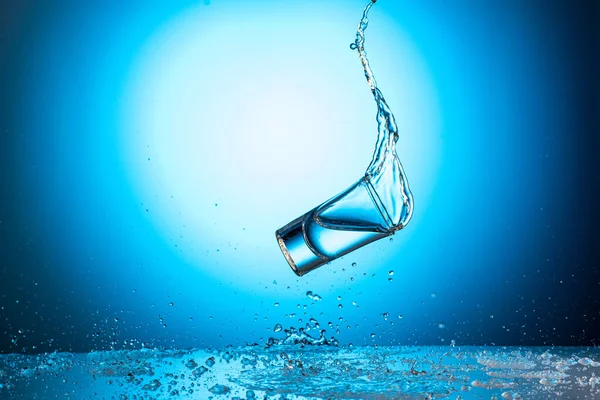 Spadające Skaczące Szkło Odrobiną Wody Lub Wódki Niebieskim Tle Gradientowym — Zdjęcie stockowe