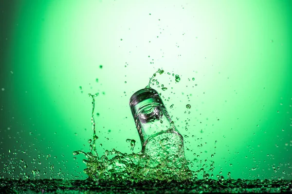 splash in the falling glass with absinthe and vodka on a green gradient background