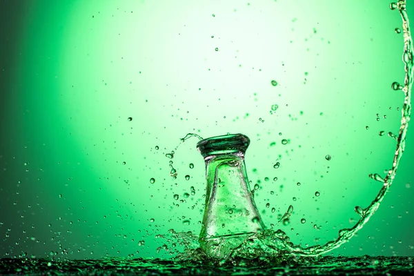 splash in the falling glass with absinthe and vodka on a green gradient background