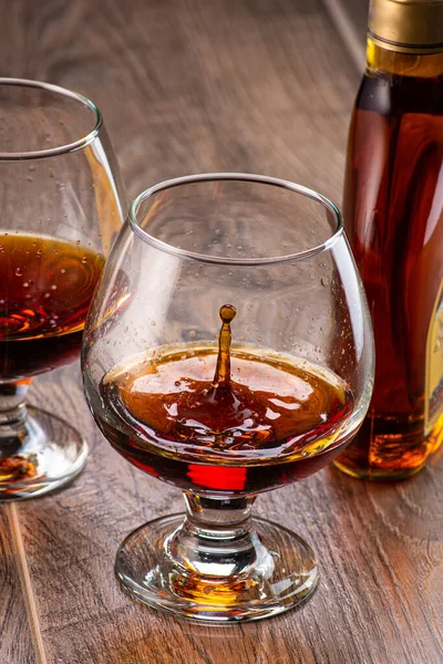 Due Bicchieri Con Cognac Spruzzi Accanto Una Bottiglia Uno Sfondo — Foto Stock
