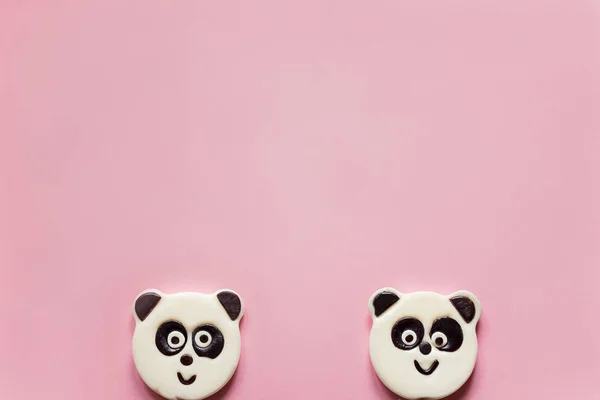 Cute panda lollipops looking out from below a pink background