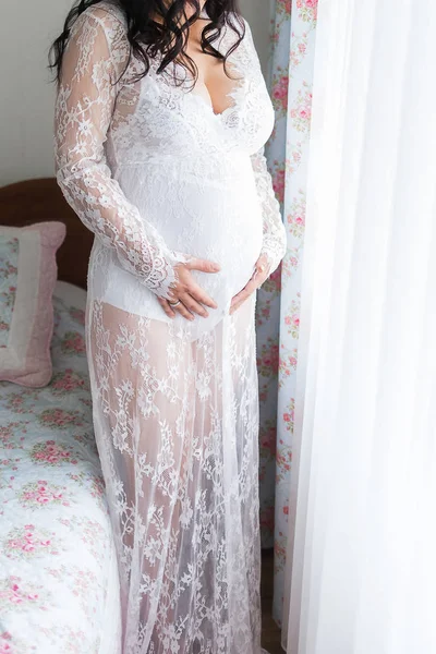 A beautiful pregnant woman stands in a long white dress and hold — Stock Photo, Image