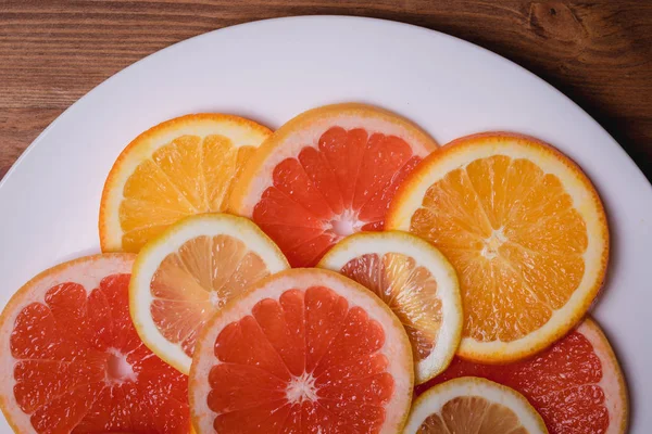 Orange grapefrukt och citron styckning i en platta på en trä bakgrund — Stockfoto