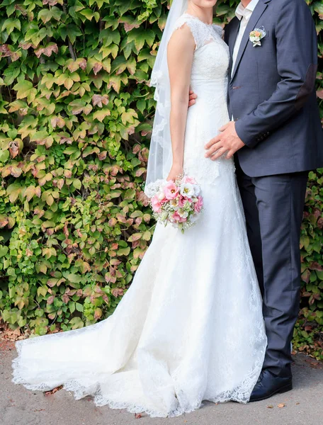 A noiva eo noivo ficar perto da parede verde — Fotografia de Stock