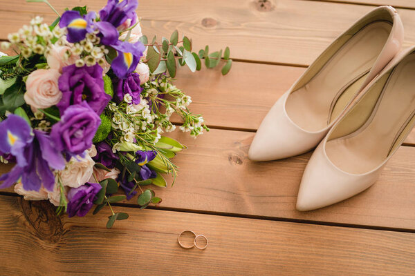 on a wooden table a wedding bouquet with green leaves, purple and white flowers, wedding rings