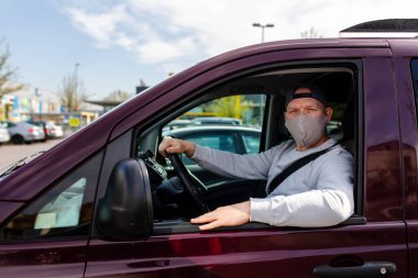 Koruyucu maskeli bir adam araba kullanıyor. Koruyucu maskeli bir adam araba sürerken eczaneye gider. Gri kazaklı bir adam arabada oturuyor ve koronavirüs maskesi takıyor..