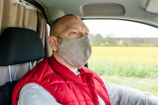 A man is sitting in a car wearing a mask. A man in a protective mask driving a car. A man goes to rest in the countryside.