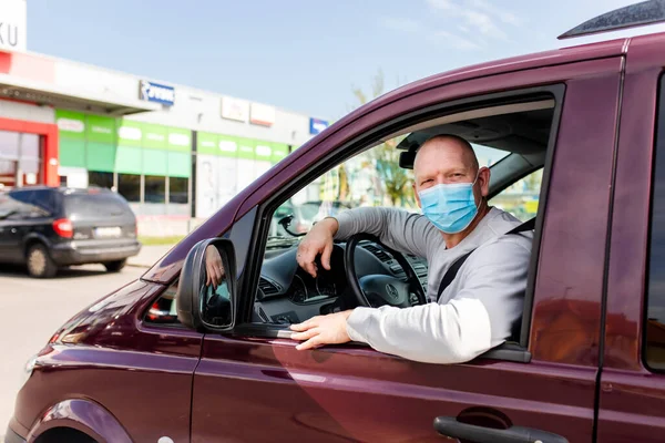 Koruyucu maskeli bir adam araba kullanıyor. Koruyucu maskeli bir adam araba sürerken eczaneye gider. Gri kazaklı bir adam arabada oturuyor ve koronavirüs maskesi takıyor..