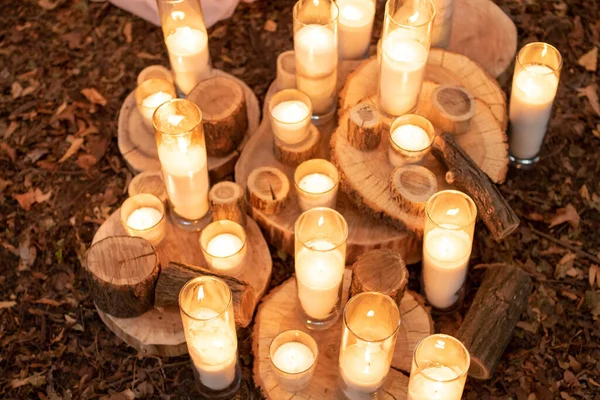 Many candles stand on the ground on wooden stands. Candles are used at a wedding ceremony in the forest, rustic style. Close-up.