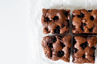 Vişneli browni yakın plan. Lezzetli bir vişneli kek kağıt üzerinde beyaz bir masanın üzerinde yatıyor. Çikolata serpiştirilmiş Brownie. Brownie evde pişirdi. Brownie DIY. Yukarıdan bak. Üst görünüm.