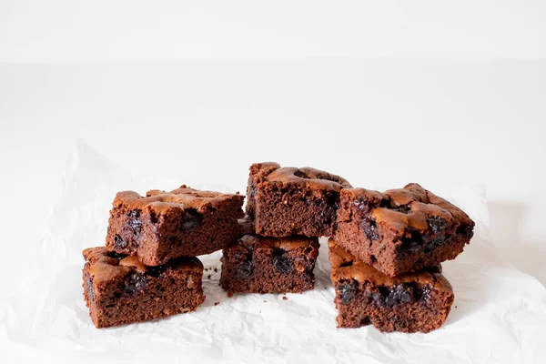 Vişneli browni yakın plan. Lezzetli bir vişneli kek kağıt üzerinde beyaz bir masanın üzerinde yatıyor. Çikolata serpiştirilmiş Brownie. Brownie evde pişirdi. Brownie DIY. Yukarıdan görüntüle.