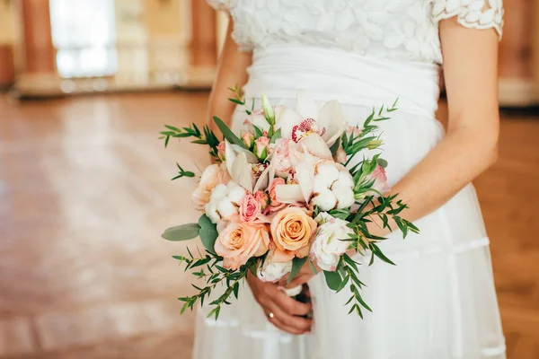 怀孕的新娘手里拿着精致的结婚花束 花束上有深绿色的叶子和白花 另一只手放在她的肚子上 白色花边裙 绿叶背景 — 图库照片