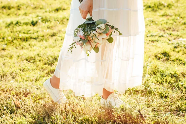 怀孕的新娘手里拿着精致的结婚花束 花束上有深绿色的叶子和白花 另一只手放在她的肚子上 白色花边裙 绿叶背景 — 图库照片