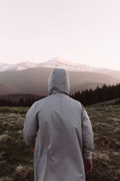 man in gray raincoat on the top of mountain background of mountains