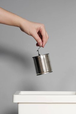 Hand puts empty tin can in the trash bin for recycling.