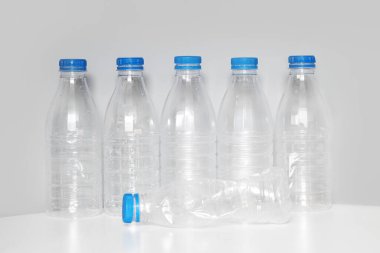 Plastic bottles with blue caps for recycling stand in a row on a white table on a gray background