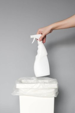 A hand puts an empty white plastic bottle of cleaning products in a recycling bin. 