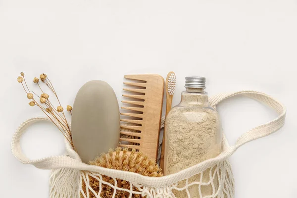 Body scrub, soap, wooden comb, beech toothbrushes, body brush in an eco shopping bag on light background